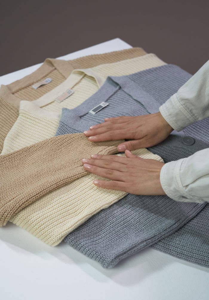 A person arranges warm cardigans in a style photo emphasizing texture and simplicity.